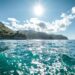 une-image-montrant-un-bateau-voguant-sur-des-eaux-turquoises-avec-une-vue-cotiere-pittoresque-en-arriere-plan-sous-un-soleil-eclatant
