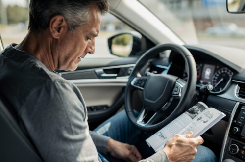 Un homme consulte le carnet d’entretien ouvert de sa voiture, tandis qu’un voyant de révision est visible sur le tableau de bord.