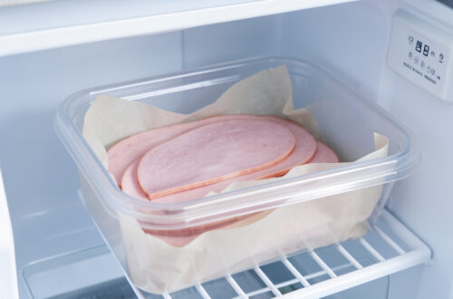 Tranches de jambon blanc séparées par du papier cuisson dans une boîte hermétique placée au congélateur.