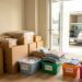 Scène de déménagement organisée avec des cartons soigneusement emballés, des fournitures de rangement et un camion visible devant un appartement lumineux.