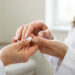 Gros plan sur la main d’une femme aux ongles pâles et blanchâtres examinée avec douceur par une médecin dans un cabinet médical.