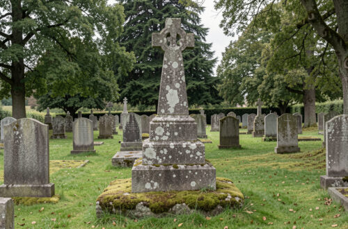 Ancien calvaire breton en granit au milieu d’un cimetière communal paisible, éclairé par une lumière douce et sans présence humaine.