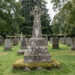 Ancien calvaire breton en granit au milieu d’un cimetière communal paisible, éclairé par une lumière douce et sans présence humaine.
