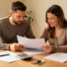Un homme et une femme examinent ensemble un dossier de prêt immobilier sur une table, entourés de documents vierges, d’une calculatrice et de clés de logement.